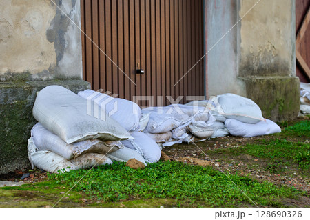 Sandbags stacked in front of door to protect building from flood water. Emergency defense measure against storm damage and natural disaster in urban residential area Sandbags stacked in front of door to protect building from flood water. Emergency defense measure against storm damage and natural disaster in urban residential area 128690326