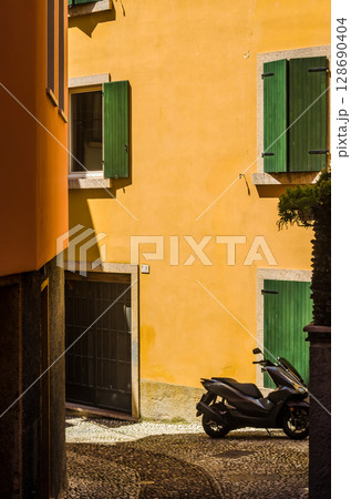 Yellow stucco wall with green shutters and parked scooter in Italian alley at noon. High quality photo Yellow stucco wall with green shutters and parked scooter in Italian alley at noon. High quality photo 128690404