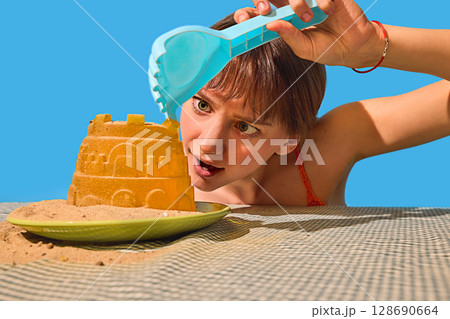 Curious woman inspecting sandcastle with toy claw on surreal table with intense expression 128690664