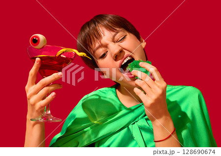 Woman biting green jelly with cocktail and gummy eyeball in humorous food setting 128690674