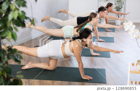 Asian girl performs bird dog pose, dandayamana hanumanasana, balancing table pose, group class Asian girl performs bird dog pose, dandayamana hanumanasana, balancing table pose, group class 128690855