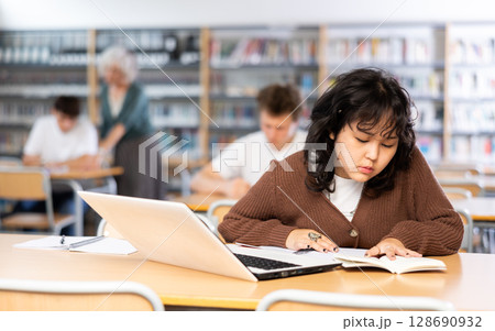 Schoolgirl studies on a laptop and writes notes in a copybook Schoolgirl studies on a laptop and writes notes in a copybook 128690932