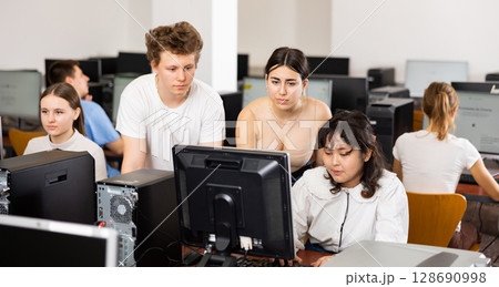 Serious students explaining the topic to female friend while she is studying computer science on the PC in the classroom Serious students explaining the topic to female friend while she is studying computer science on the PC in the classroom 128690998