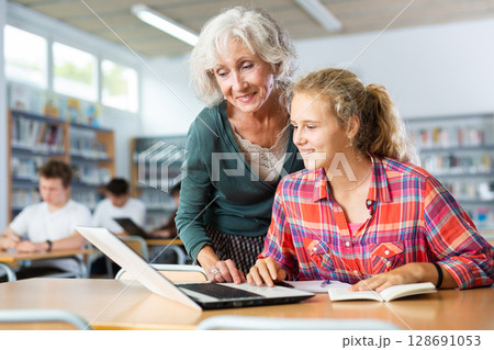 Mature female teacher working with schoolgirl in computer class of library 128691053