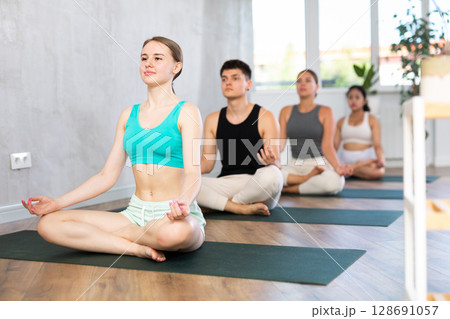Young yogi girl and man making yoga meditation in lotus pose in fitness studio 128691057