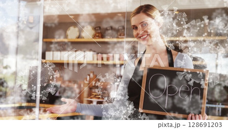 Barista holding Open chalkboard sign behind counter in cafe, with virus decals, jars and cups 128691203