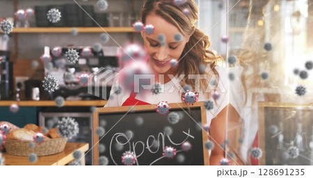Smiling barista holding open sign at café counter, with bread basket, espresso machine and virus Smiling barista holding open sign at café counter, with bread basket, espresso machine and virus 128691235