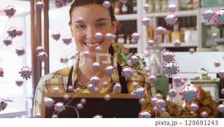 Smiling barista holding blank chalkboard sign behind café counter, with floating coronavirus icons Smiling barista holding blank chalkboard sign behind café counter, with floating coronavirus icons 128691243