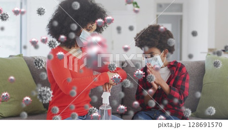 Pumping mother and son sanitizing hands in home living room, with spray bottle, 3D virus graphics 128691570