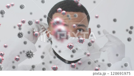 Adjusting man in protective suit and gloves fixing mask straps in studio, with virus particles 128691975