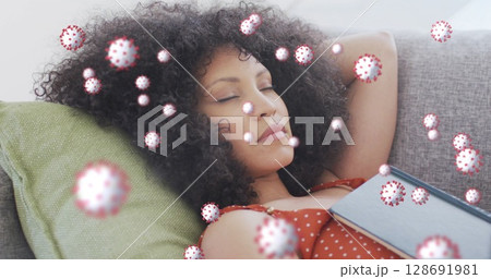 Lying woman in orange polka-dot dress holding book on sofa at home, with floating virus overlay Lying woman in orange polka-dot dress holding book on sofa at home, with floating virus overlay 128691981