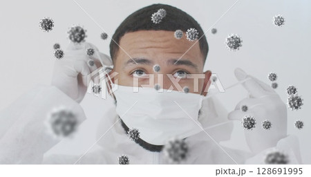 Man wearing white coverall and latex gloves, adjusting surgical mask in lab, with virus particles Man wearing white coverall and latex gloves, adjusting surgical mask in lab, with virus particles 128691995