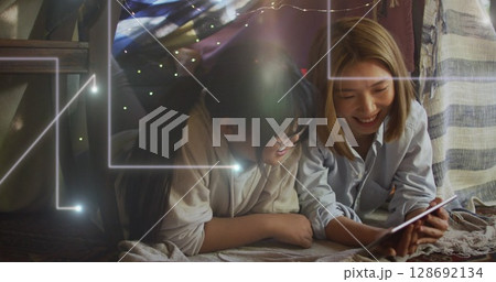 Image of lights falling over happy asian mother and daughter using tablet 128692134