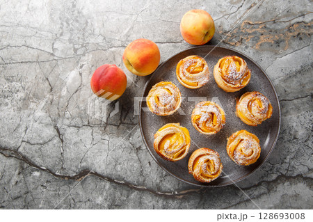 Peach roses mini tarts muffins made of puff pastry with powdered sugar close-up on a plate. horizontal top view 128693008