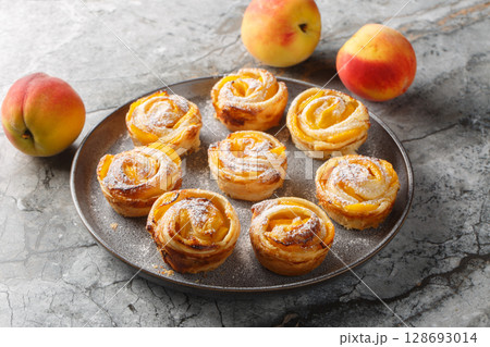Peach roses mini tarts muffins made of puff pastry with powdered sugar close-up on a plate. horizontal Peach roses mini tarts muffins made of puff pastry with powdered sugar close-up on a plate. horizontal 128693014