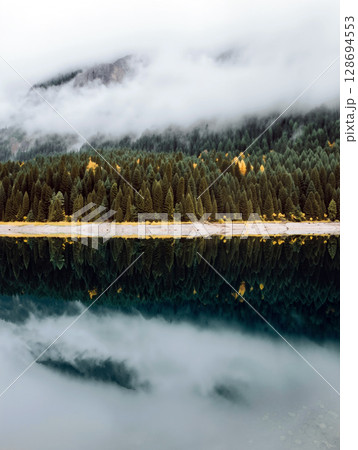 Serene lake reflecting mountains and forests in a misty landscape near dawn Serene lake reflecting mountains and forests in a misty landscape near dawn 128694553