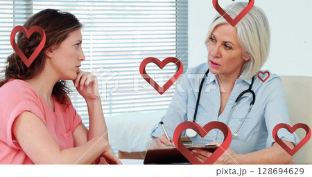 Image of hearts falling over caucasian female doctor talking with patient 128694629