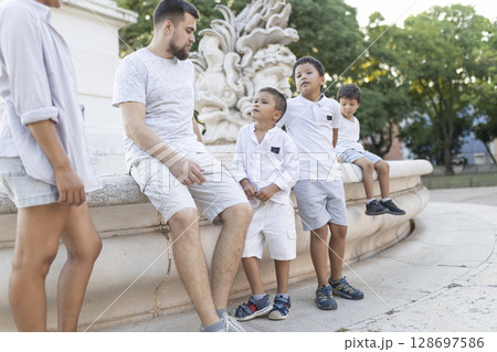 Family relaxing on fountain in city park during summer vacation Family relaxing on fountain in city park during summer vacation 128697586
