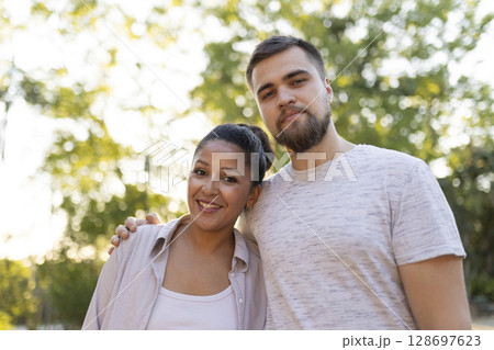 Interracial couple smiling and embracing in a park 128697623