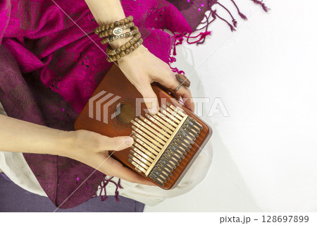 Woman holding kalimba in her hands and playing. Concept of Relaxing at home, Me time and self care and sound meditation. Woman enjoy the melodious sound of the thumb piano playing. Closeup Woman holding kalimba in her hands and playing. Concept of Relaxing at home, Me time and self care and sound meditation. Woman enjoy the melodious sound of the thumb piano playing. Closeup 128697899