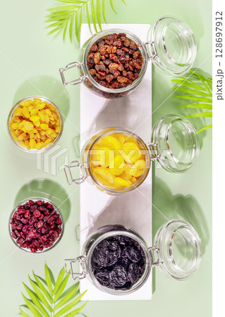 Dry fruits assortment on blue background with palm leaves. Healthy snack - mix of organic nuts and dry fruits. Vegan and vegetarian products. Healthy food. Flat lay Dry fruits assortment on blue background with palm leaves. Healthy snack - mix of organic nuts and dry fruits. Vegan and vegetarian products. Healthy food. Flat lay 128697912