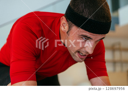 A triathlete riding a triathlon bike on a machine simulation in a modern living room. Training during pandemic conditions. 128697956