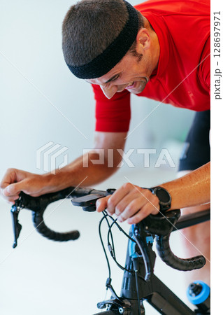 A triathlete riding a triathlon bike on a machine simulation in a modern living room. Training during pandemic conditions. 128697971