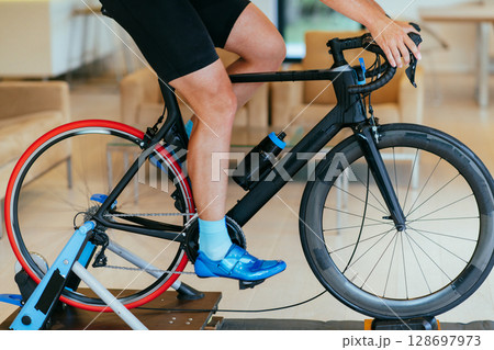 A triathlete riding a triathlon bike on a machine simulation in a modern living room. Training during pandemic conditions. A triathlete riding a triathlon bike on a machine simulation in a modern living room. Training during pandemic conditions. 128697973