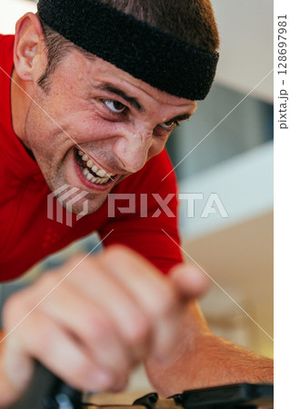 A triathlete riding a triathlon bike on a machine simulation in a modern living room. Training during pandemic conditions. 128697981