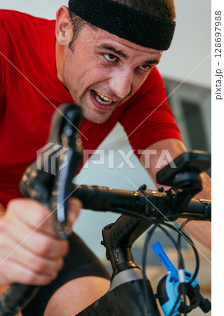 A triathlete riding a triathlon bike on a machine simulation in a modern living room. Training during pandemic conditions. 128697988
