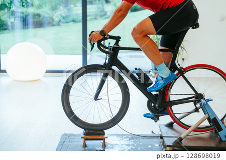 A triathlete riding a triathlon bike on a machine simulation in a modern living room. Training during pandemic conditions. 128698019