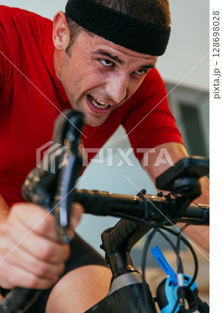 A triathlete riding a triathlon bike on a machine simulation in a modern living room. Training during pandemic conditions. A triathlete riding a triathlon bike on a machine simulation in a modern living room. Training during pandemic conditions. 128698028