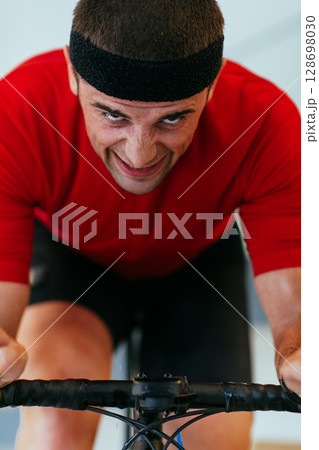 A triathlete riding a triathlon bike on a machine simulation in a modern living room. Training during pandemic conditions. A triathlete riding a triathlon bike on a machine simulation in a modern living room. Training during pandemic conditions. 128698030