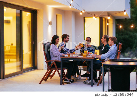 A group of young diverse people having dinner on the terrace of a modern house in the evening. Fun for friends and family. Celebration of holidays, weddings with barbecue A group of young diverse people having dinner on the terrace of a modern house in the evening. Fun for friends and family. Celebration of holidays, weddings with barbecue 128698044