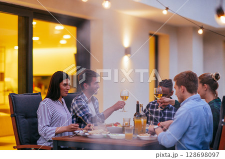 A group of young diverse people having dinner on the terrace of a modern house in the evening. Fun for friends and family. Celebration of holidays, weddings with barbecue A group of young diverse people having dinner on the terrace of a modern house in the evening. Fun for friends and family. Celebration of holidays, weddings with barbecue 128698097