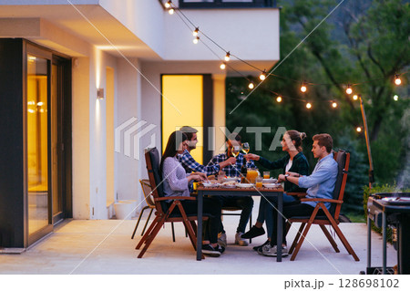 A group of young diverse people having dinner on the terrace of a modern house in the evening. Fun for friends and family. Celebration of holidays, weddings with barbecue 128698102
