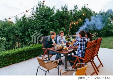 A group of young diverse people having dinner on the terrace of a modern house in the evening. Fun for friends and family. Celebration of holidays, weddings with barbecue 128698138