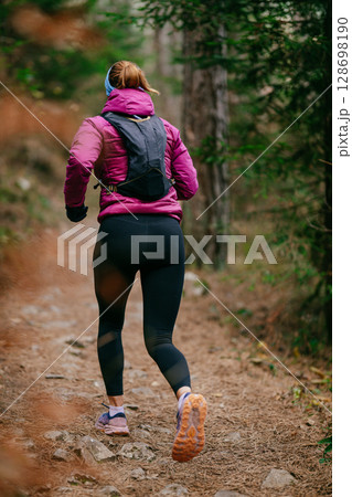 Determined Female Athlete Running with Focus Through a Dense Pine Forest, Embracing Strength and Nature 128698190