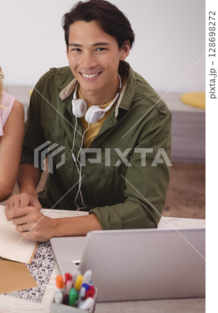 Smiling man with headphones working on laptop at creative office desk Smiling man with headphones working on laptop at creative office desk 128698272