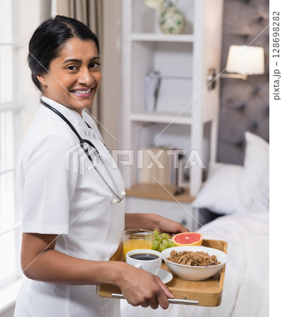 Smiling nurse serving healthy breakfast in cozy bedroom, promoting wellness care 128698282