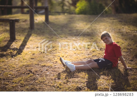 Smiling child in red shirt sitting on grass in sunny park, copy space 128698283