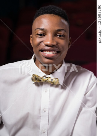Smiling young man in theater wearing stylish bow tie, enjoying moment Smiling young man in theater wearing stylish bow tie, enjoying moment 128698290