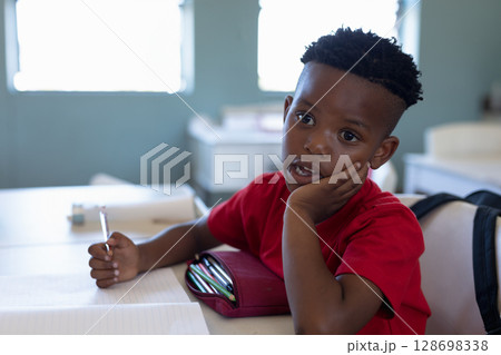In school, young boy in red shirt daydreaming during class at desk 128698338