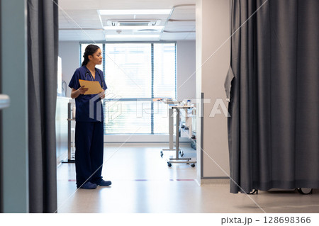 Nurse in hospital corridor holding patient files, preparing for rounds, copy space 128698366