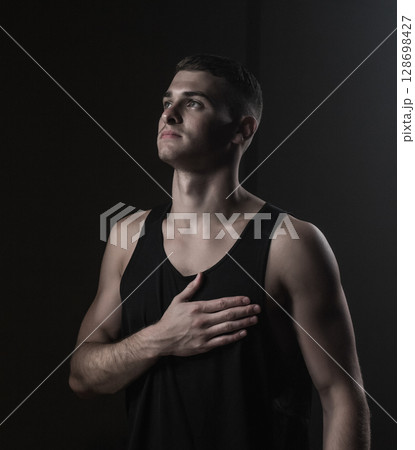 Athlete in black tank top looking up, hand on chest, feeling determined Athlete in black tank top looking up, hand on chest, feeling determined 128698427