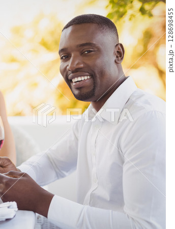 Smiling man enjoying outdoor dining with friends, holding glass of wine 128698455
