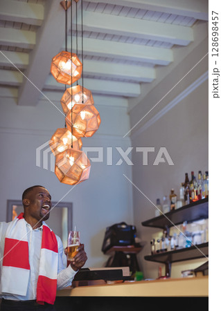 Man enjoying drink at bar, wearing scarf, smiling under modern pendant lights, copy space 128698457