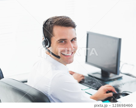 Smiling businessman using headset and computer at office desk, providing support 128698460