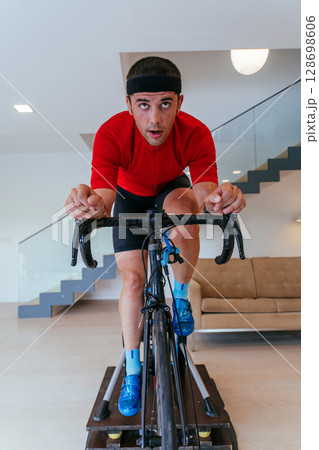 A triathlete riding a triathlon bike on a machine simulation in a modern living room. Training during pandemic conditions. A triathlete riding a triathlon bike on a machine simulation in a modern living room. Training during pandemic conditions. 128698606