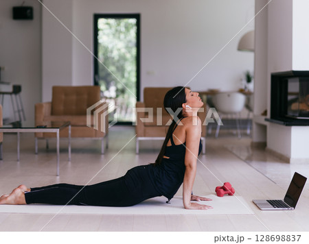 Young Beautiful Female Exercising, Stretching and Practising Yoga with Trainer via Video Call Conference in Bright Sunny House. Healthy Lifestyle, Wellbeing and Mindfulness Concept. 128698837